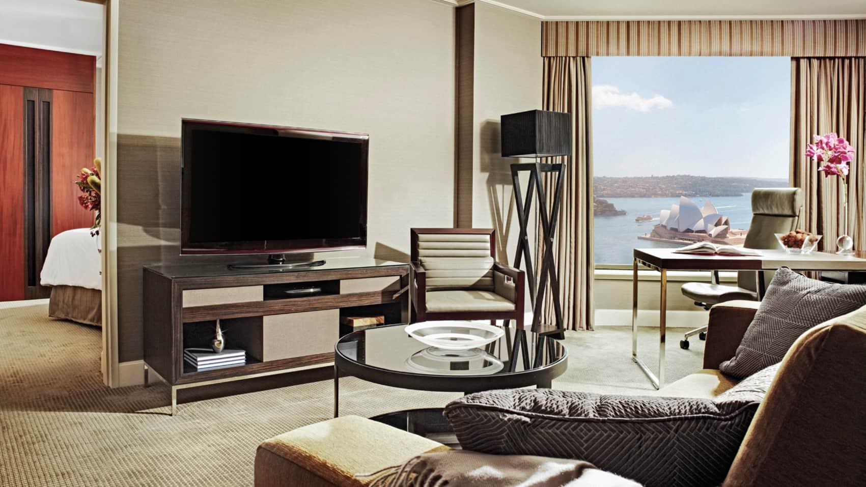 Four Seasons Hotel Сидней Экстерьер фото The photo shows a modern hotel room with a spacious and elegant design. It features a large flat-screen television situated on a wooden console. There’s a comfortable armchair next to the TV, and a round glass coffee table is positioned in front of a