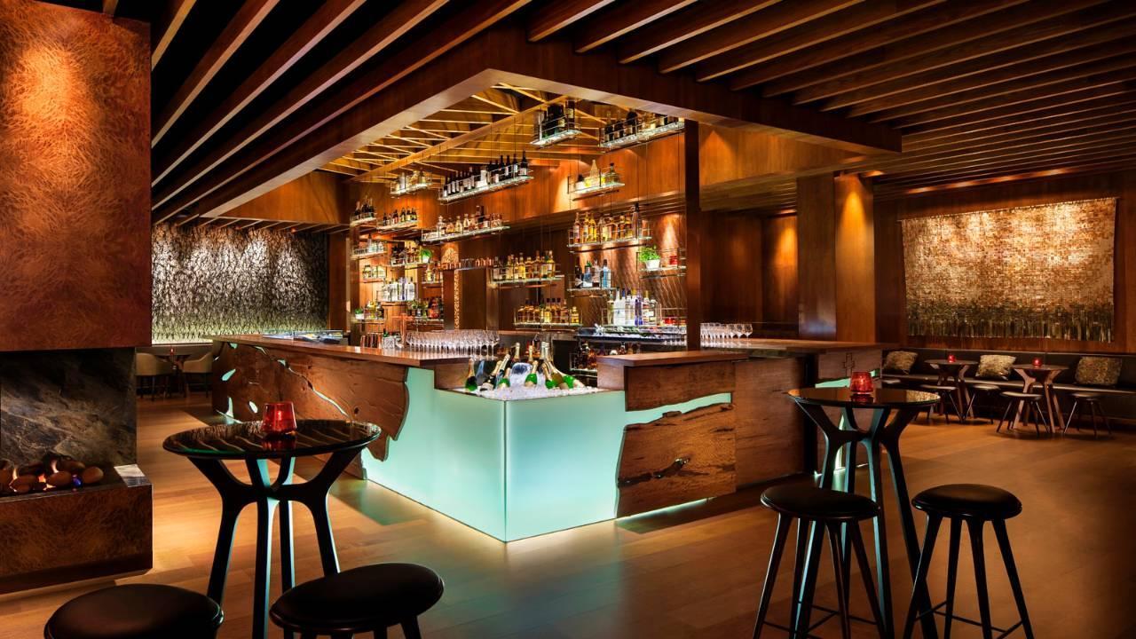 Four Seasons Hotel Сидней Экстерьер фото The image showcases a stylish, contemporary bar interior. The bar itself features a sleek design with a wooden structure and illuminated sections, creating a warm ambiance. Behind the bar, shelves are filled with a variety of bottles, indicating a we