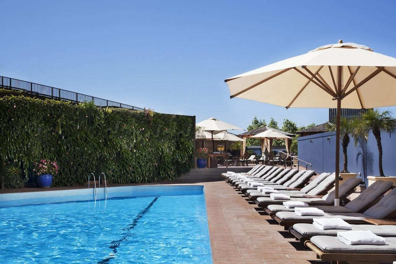 Four Seasons Hotel Сидней Удобства фото The photo shows a swimming pool surrounded by lounge chairs and large umbrellas. The pool itself has clear blue water, and there is a green wall of lush vegetation nearby, providing a natural backdrop. In the background, there are additional shaded s